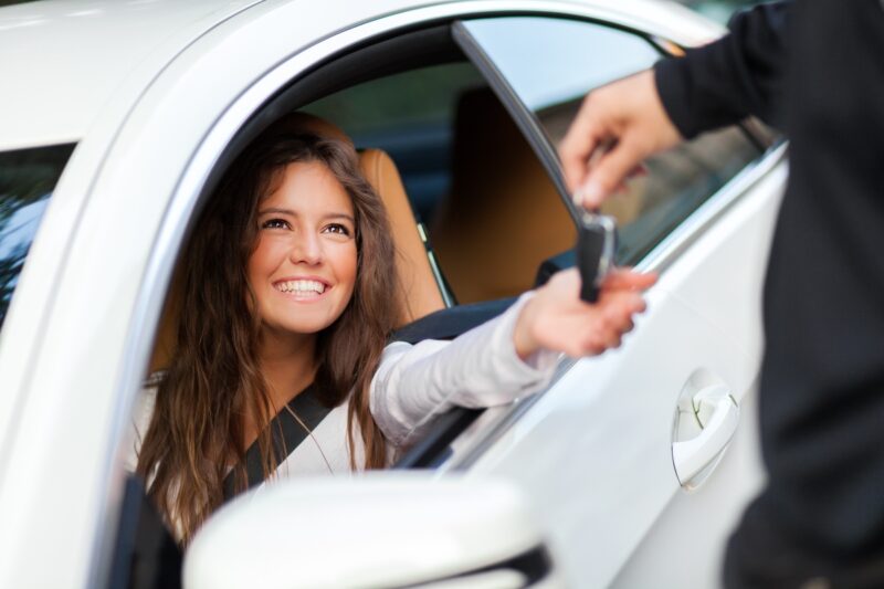 Ragazza sorridente seduta nella sua nuova auto mentre riceve le chiavi