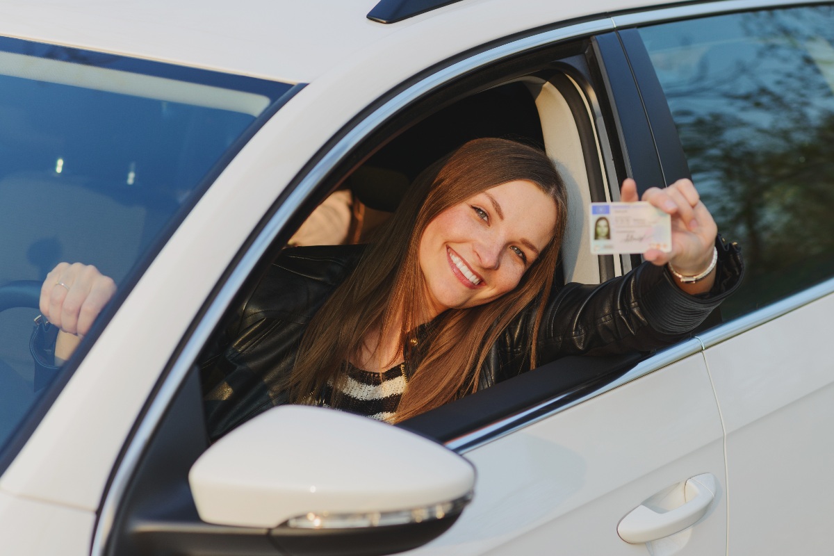 Ragazza sorridente seduta nella sua auto nuova mostra orgogliosa la patente