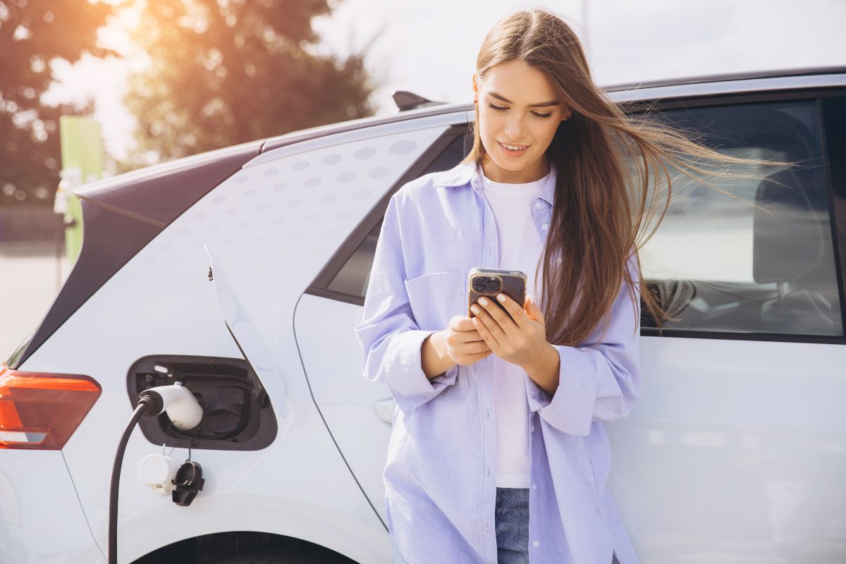 Ragazza al telefono attende ricarica dell'auto elettrica