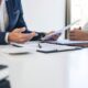 Due persone esaminano documenti cartacei su una scrivania in ufficio.