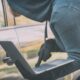 Un uomo con cappuccio e guanti neri manovra un computer portatile accanto alla maniglia di un'auto.
