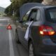 Auto ferma a bordo strada con panno bianco al finestrino, quattro frecce e triangolo di emergenza.